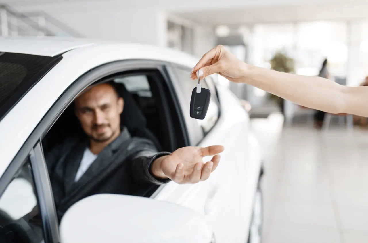 zadowolony mężczyzna odbierający kluczyk do właśnie kupionego samochodu