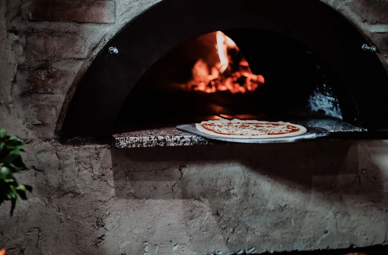 świeża pizza wkładana do dużego pieca ogrodowego