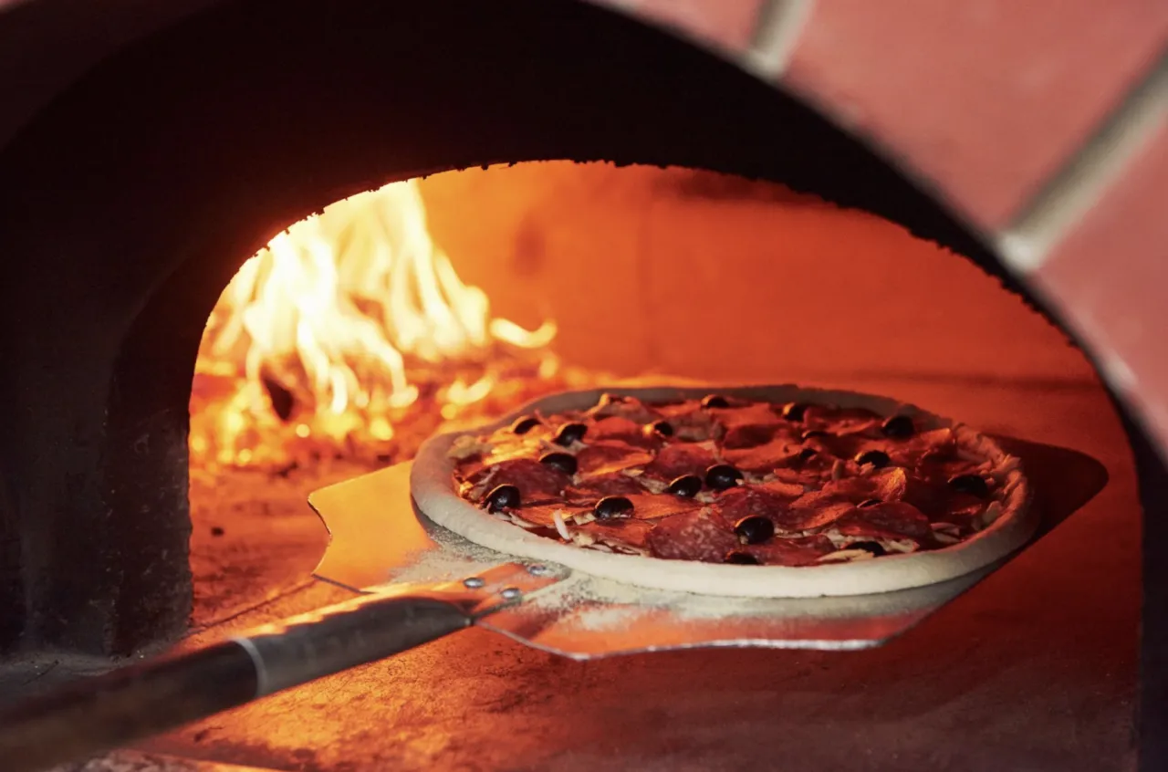 pizza wkładana do rozgrzanego pieca opalanego drewnem