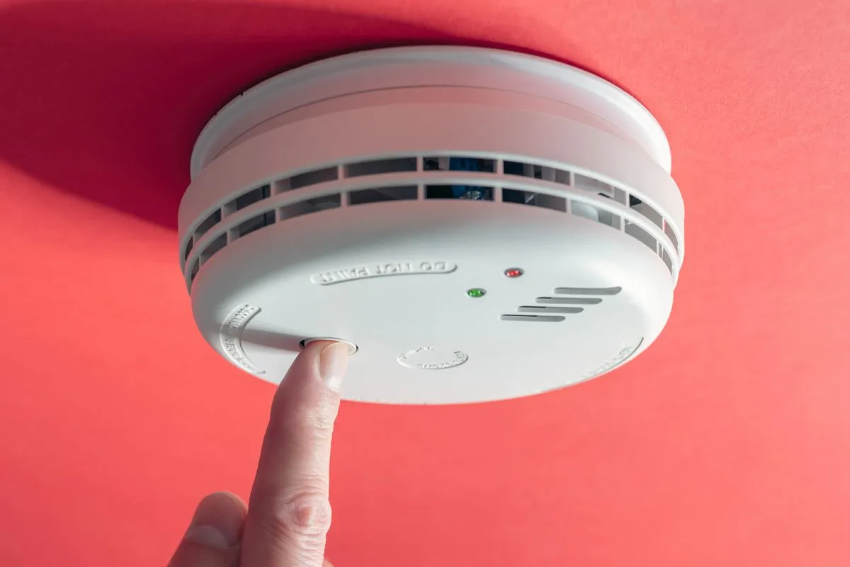 Palec naciska przycisk testowy na białym czujniku czadu zamontowanym na czerwonym suficie. Czujnik czadu kiedy potrzebny, zapewnia bezpieczeństwo.