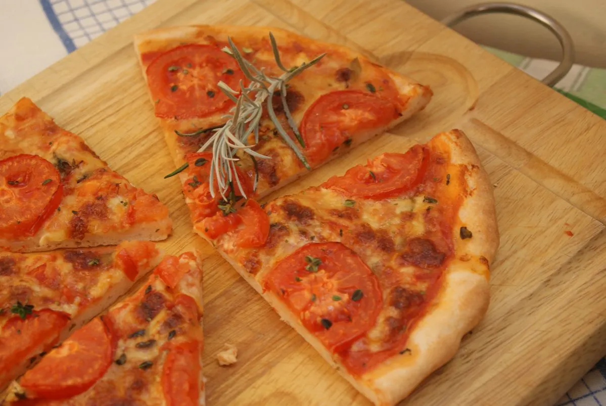 Kawałki pysznej pizzy bezglutenowej z pomidorami i rozmarynem na desce. Idealny przepis na pizzę bezglutenową.