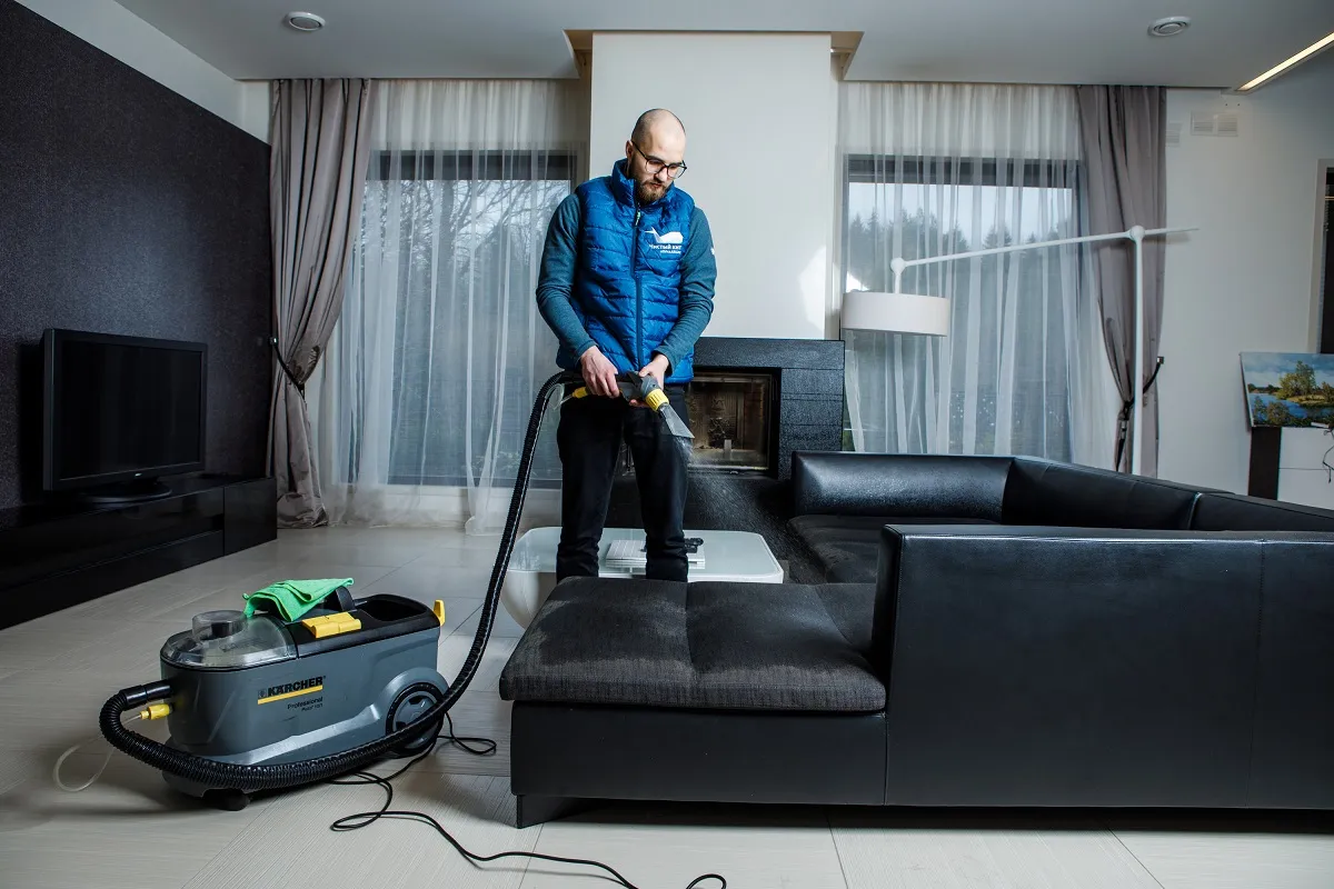 Mężczyzna używa odkurzacza piorącego, by pokazać, jak usunąć plamy z wymiocin z kanapy.