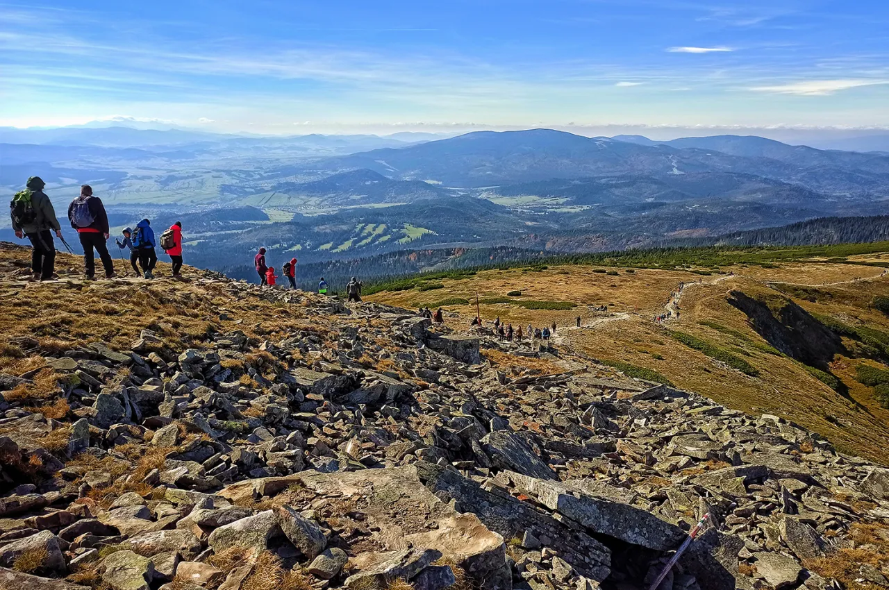 Grupa turyst&oacute;w na skalistym szlaku, podziwiająca panoramę Beskid&oacute;w. Planujesz wycieczkę? Babia G&oacute;ra jak dojechać, szukaj informacji o szlakach!