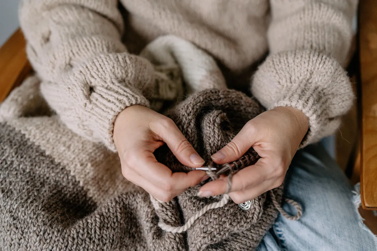Ręce dziergają sweter z grubej wł&oacute;czki. To początek tworzenia własnego, ciepłego ubrania, idealnego na zimowe wieczory.