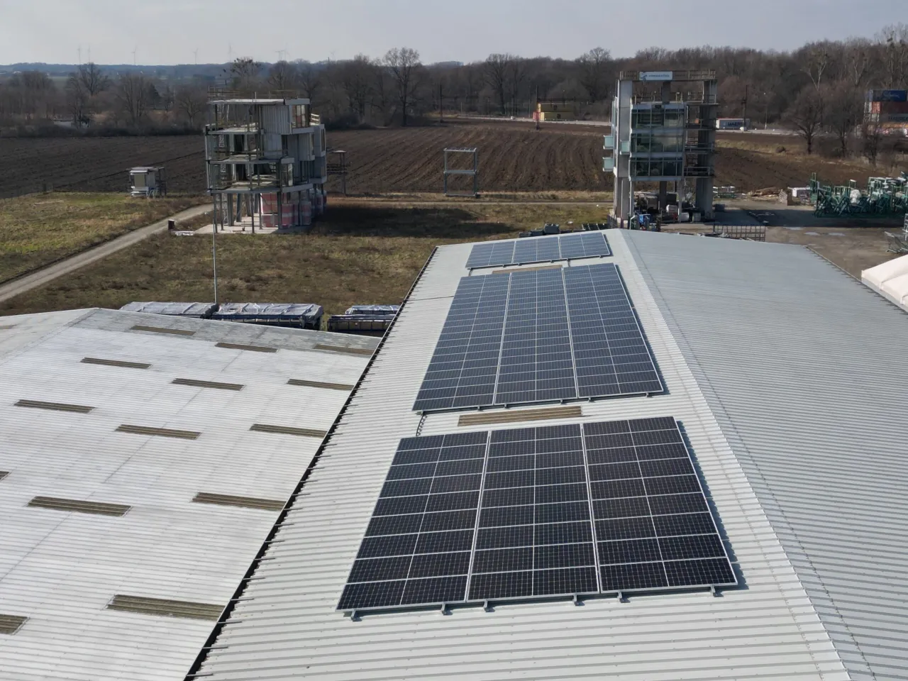 Panele fotowoltaiczne na dachu magazynu. W tle budowa, pola i wiatraki. Od kiedy 150 kw bez pozwolenia na budowę?