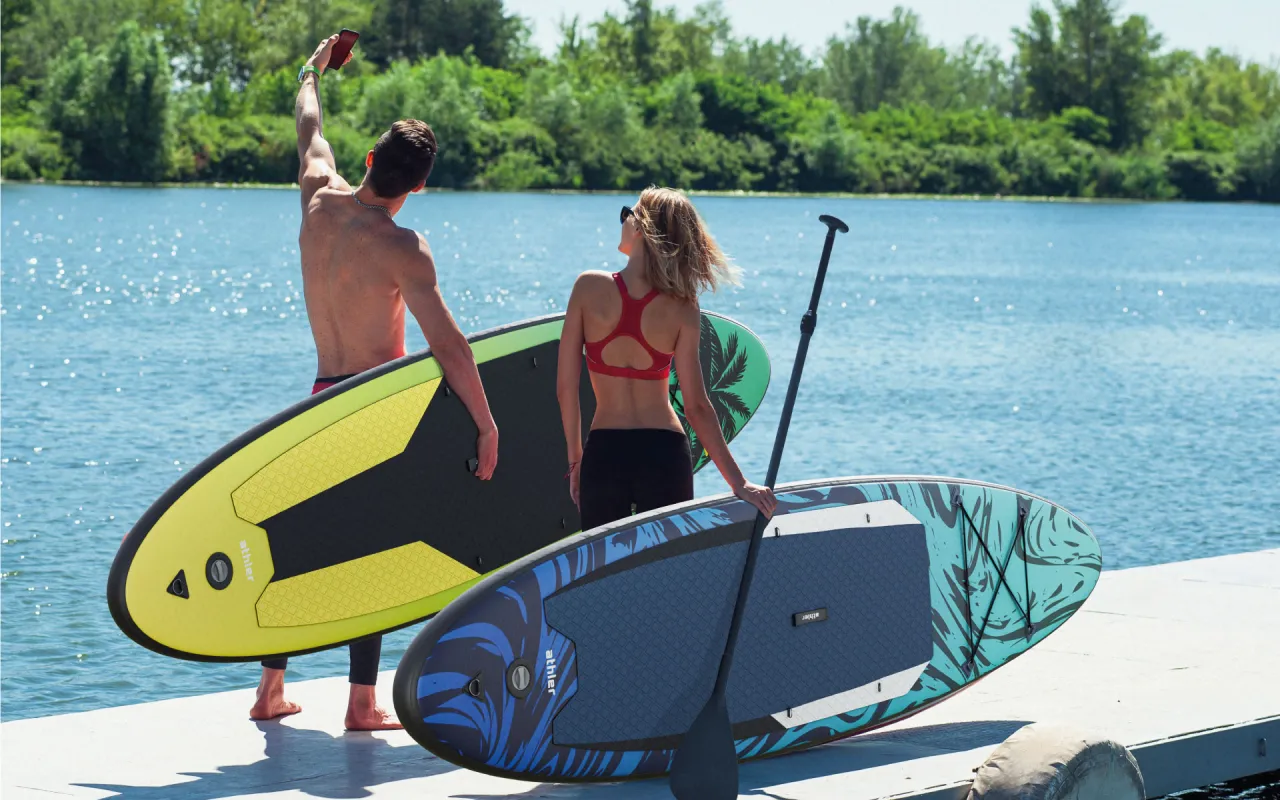 Para szykuje się na wodną przygodę z deskami do pływania z wiosłem. Słońce odbija się od wody, a oni gotowi są na relaks.