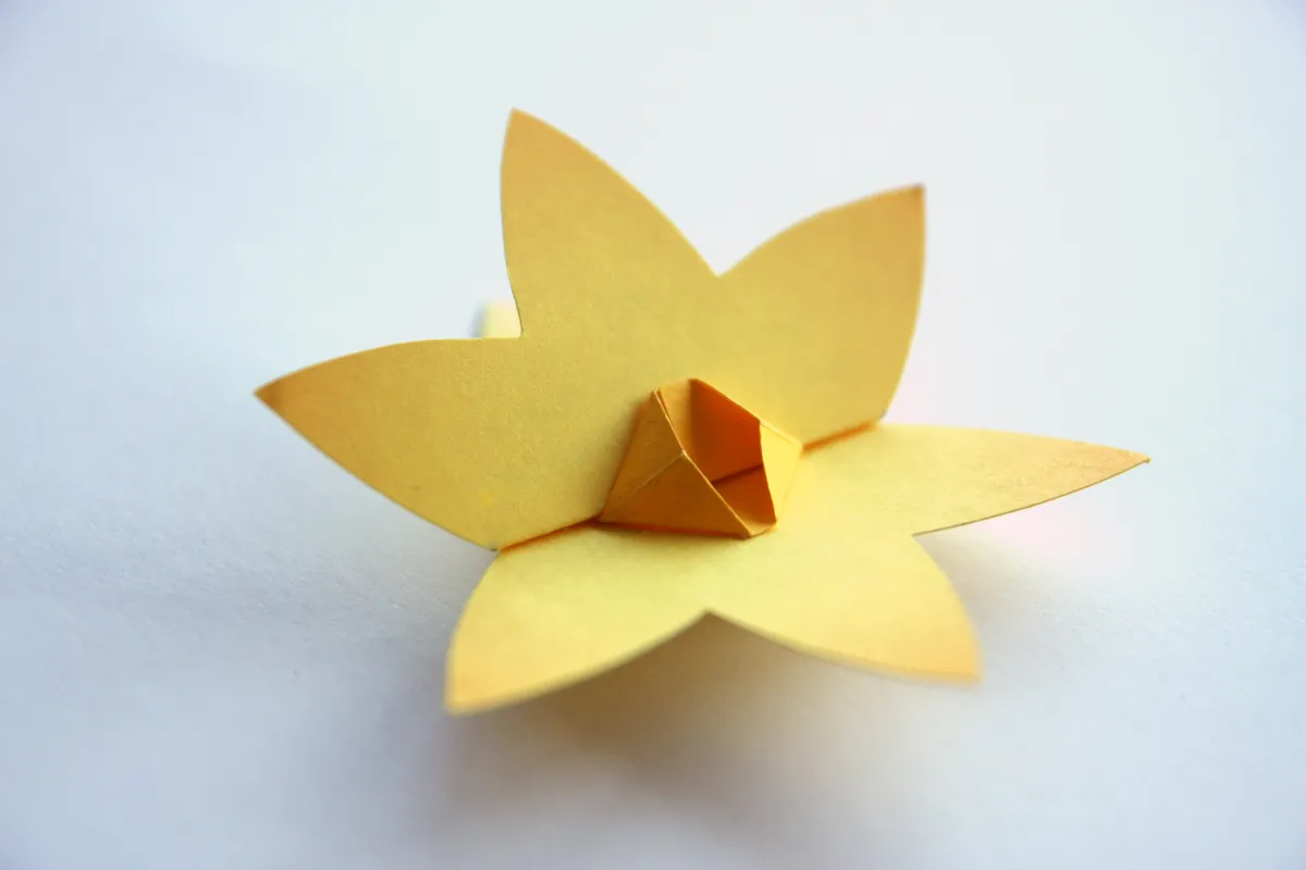 Żółty, papierowy żonkil, symbolizujący nadzieję i nowy początek, delikatnie spoczywa na białym tle.