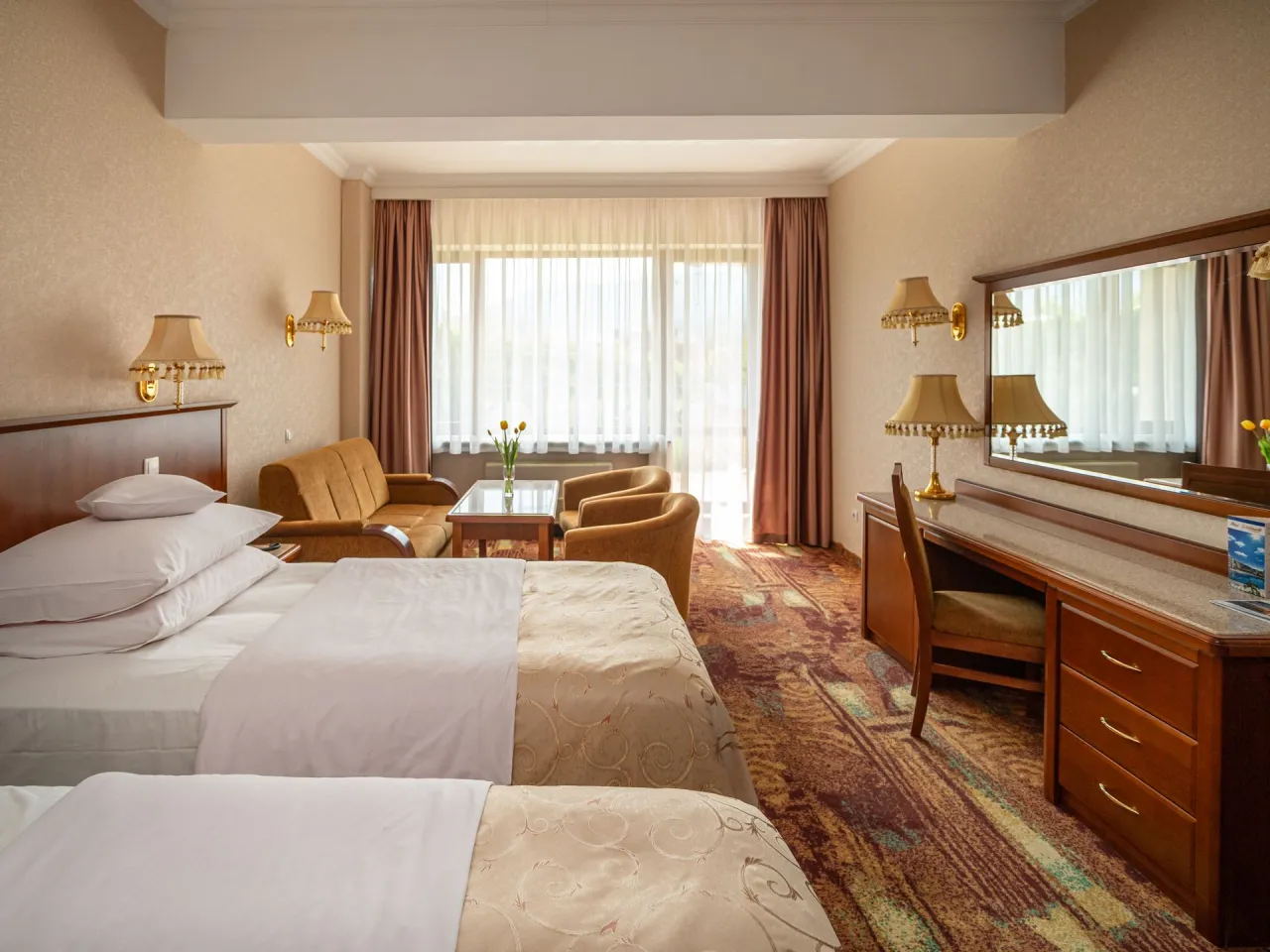 Pokój hotelowy z dwoma łóżkami, kanapą i biurkiem. Zastanawiasz się, ile kosztuje doba w hotelu Gołębiewski dla dwóch osób?