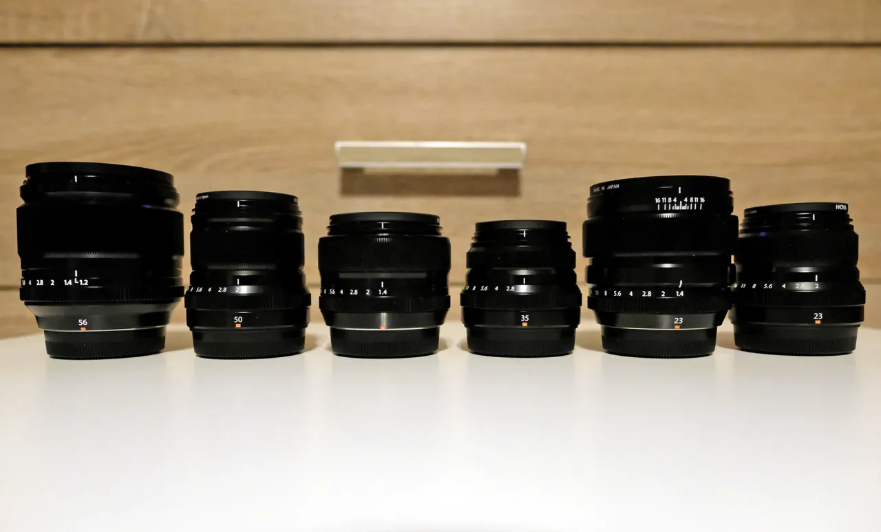 Sześć obiektyw&oacute;w do aparatu Fujifilm lustrzanka, ustawionych w rzędzie na białej powierzchni.
