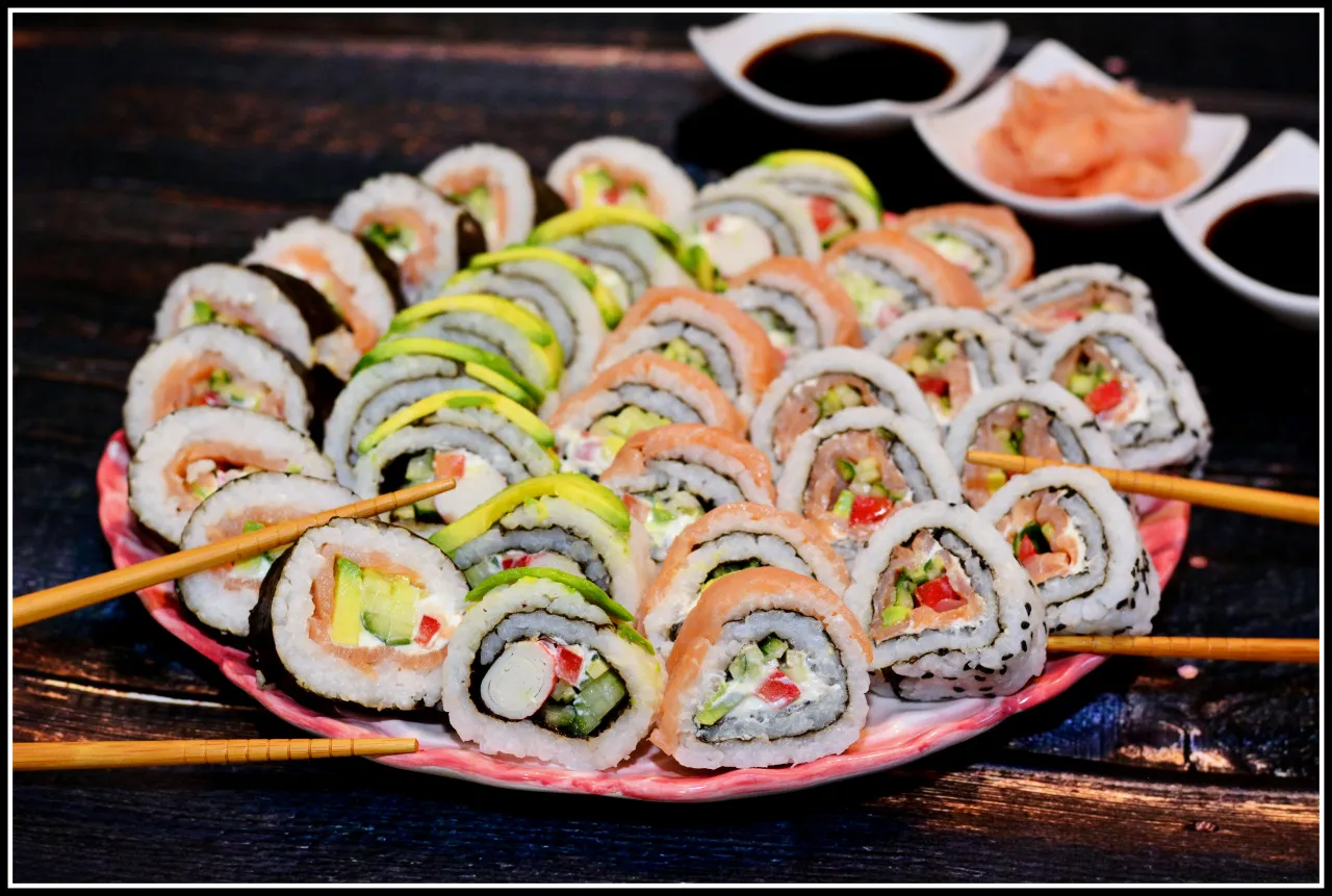 Talerz pełen kolorowych roladek sushi uramaki z łososiem, awokado i warzywami. Patyczki do jedzenia czekają na smakoszy.