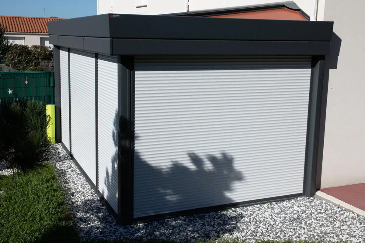 Nowoczesna wiata z białymi roletami zewnętrznymi natynkowymi, otoczona żwirem i zielenią.