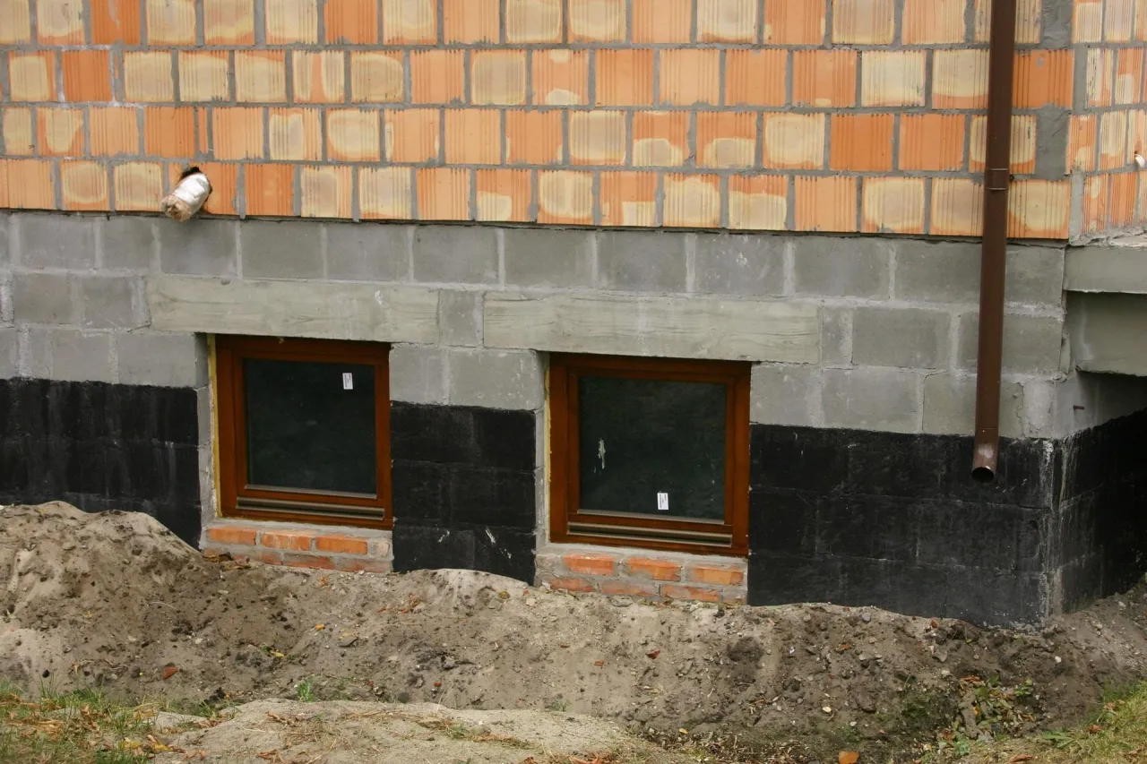Fundamenty starego domu z oknami i izolacją przeciwwilgociową. Rozważasz, czy ocieplać fundamenty w starym domu?