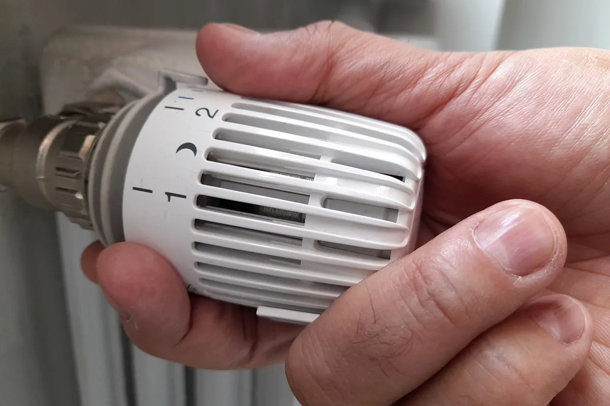 Ręka kręci termostatem grzejnika, ustawiając temperaturę. Czekamy, aż włączą ogrzewanie w blokach.