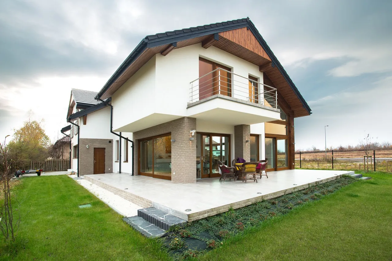 Nowoczesny dom z białym tynkiem, drewnianymi elementami i dużymi oknami. Elegancki akryl do elewacji podkreśla jego styl.