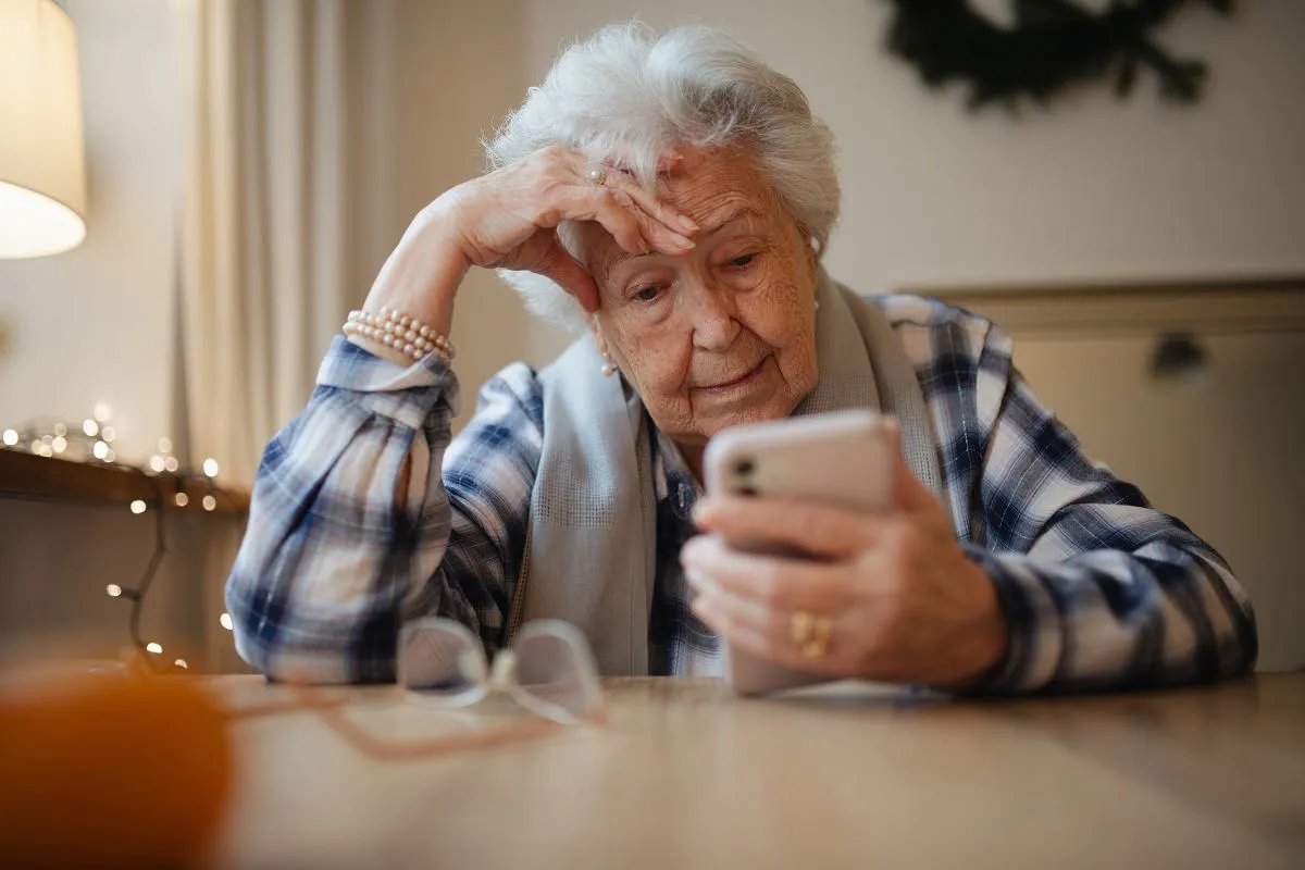Starsza pani zamyślona, trzymająca telefon. To właśnie co to senior – osoba pełna doświadczeń, korzystająca z technologii.