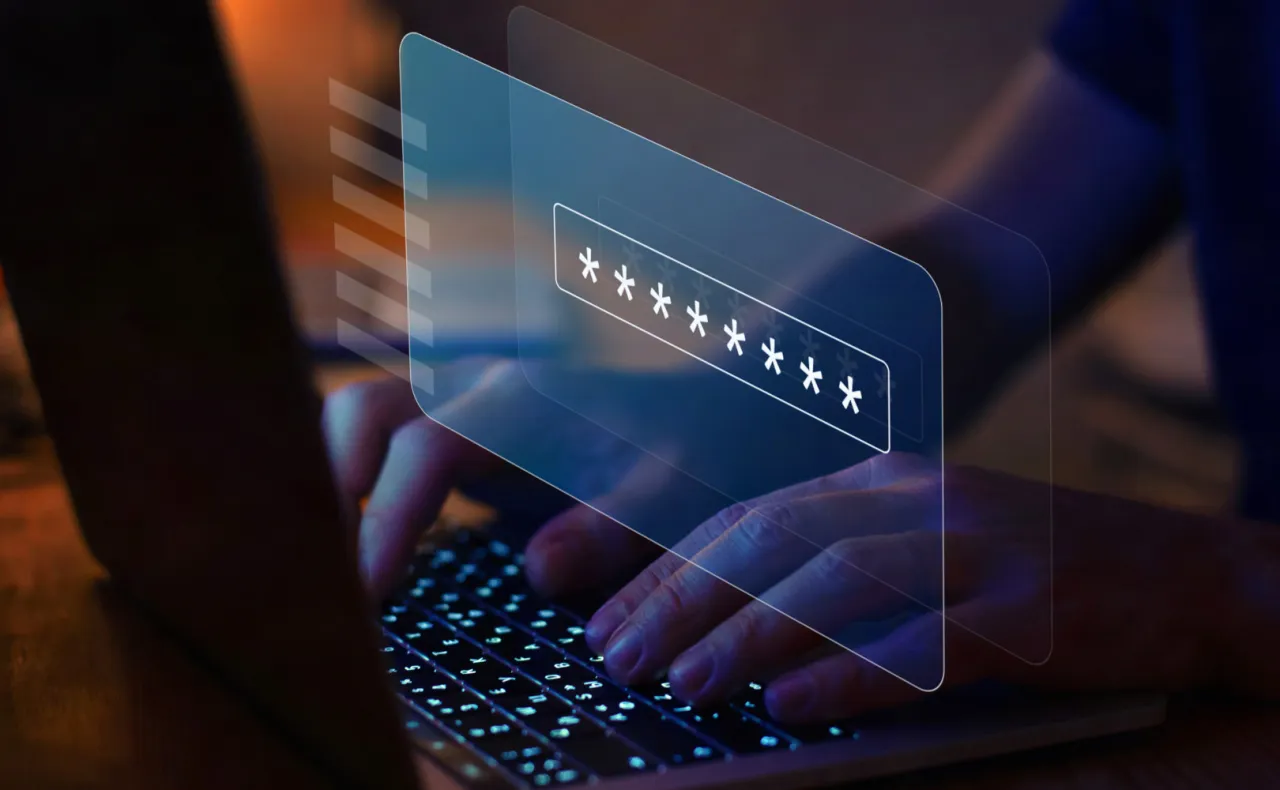 Dłonie wpisują hasło na podświetlanej klawiaturze laptopa. Wirtualny interfejs pokazuje pole z gwiazdkami, sugerując jak zmienić hasło na komputerze.
