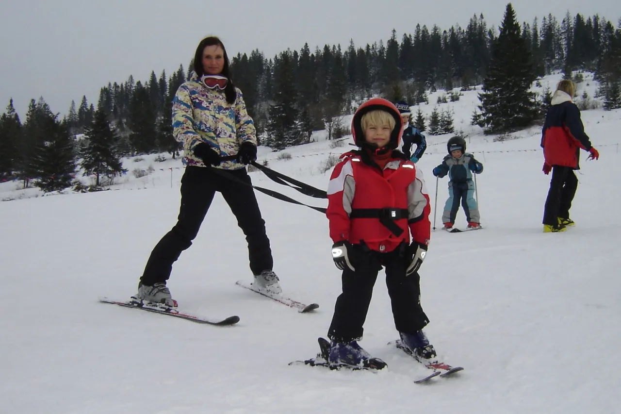 dziecko w szelkach narciarskich na stoku z rodzicem