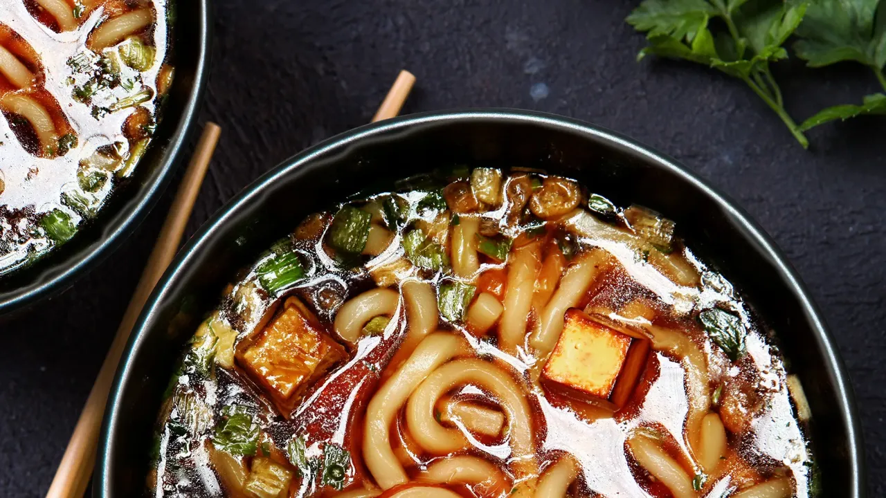 Dwie miski aromatycznej zupy udon z tofu i szczypiorkiem, gotowe do podania z pałeczkami.