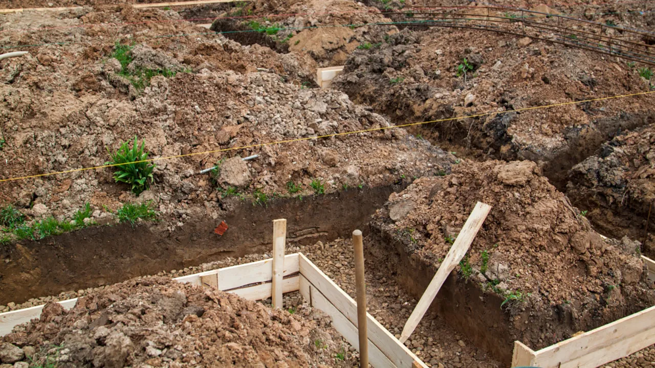 Wykonano wykop pod fundament. Widać ziemię, drewniane szalunki i zbrojenie.