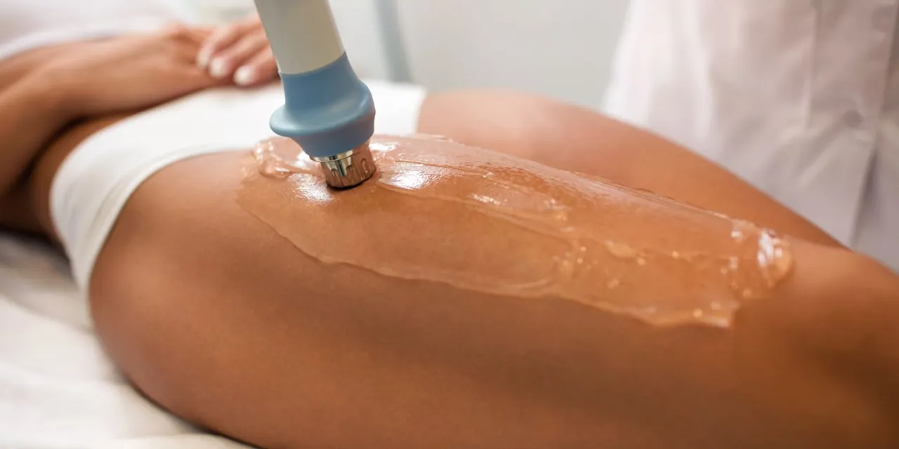 Zabieg na cellulit: urządzenie kosmetyczne z żelem na udzie kobiety, poprawiające wygląd skóry.