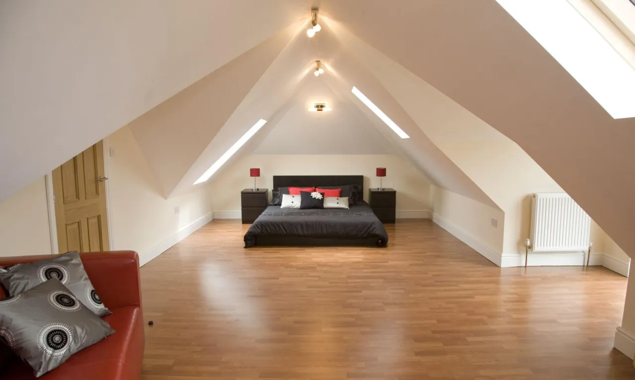 Sypialnia na poddaszu z łóżkiem, szafkami nocnymi i kanapą. Czy strych to powierzchnia użytkowa? Tak, ten wygląda na komfortowy!