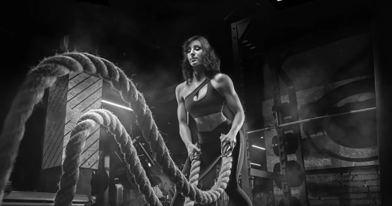 Kobieta ćwiczy z linami w siłowni. Czy crossfit warto? Intensywny trening buduje siłę i wytrzymałość.