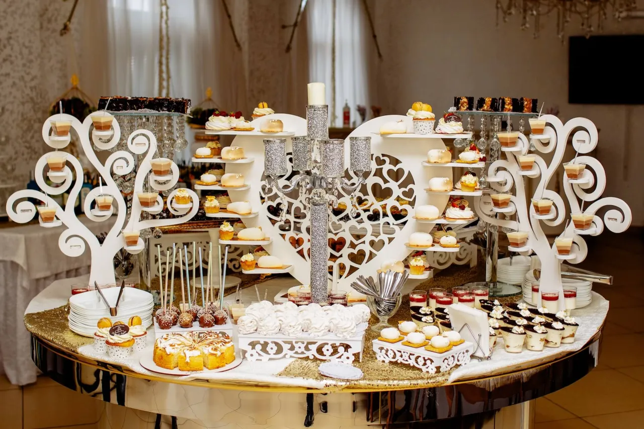 Słodki stół pełen kuszących przekąsek na komunię: babeczki, ciasta, desery w pucharkach i lizaki czekoladowe.