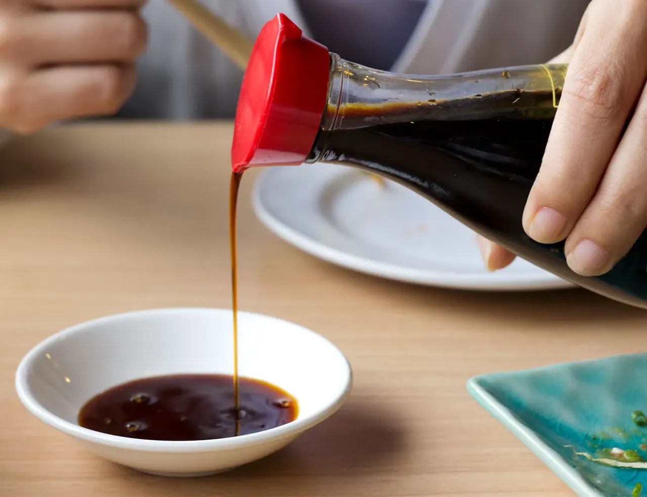 Dłoń przelewa sos sojowy do małej miseczki, idealny dodatek do sushi i innych azjatyckich potraw.