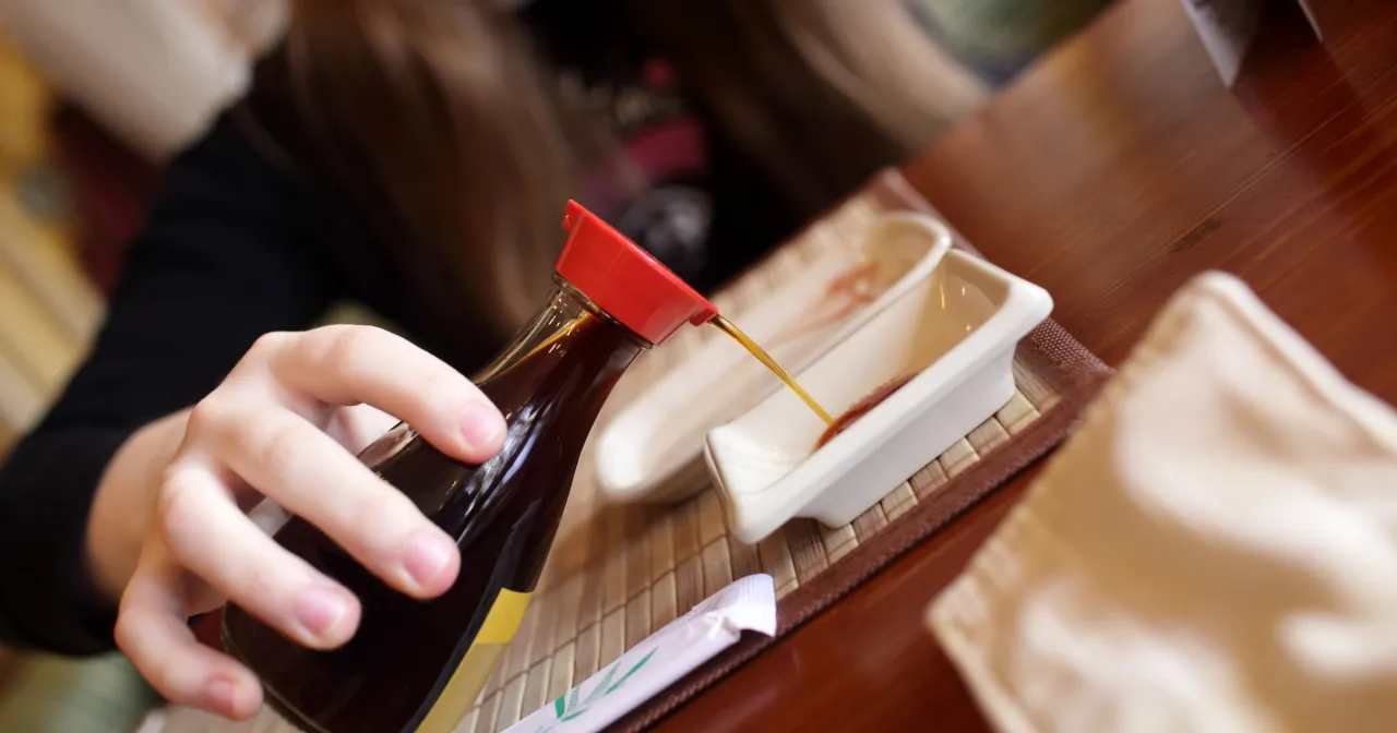 Dłoń nalewa sos sojowy do miseczki. Czy sos sojowy można zastąpić maggi? Zastanawiamy się nad smakiem.