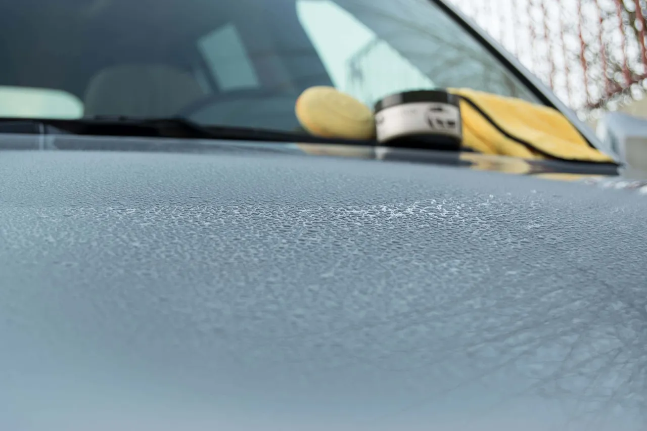 Krople wody na masce samochodu, obok słoik wosku i żółta ściereczka.