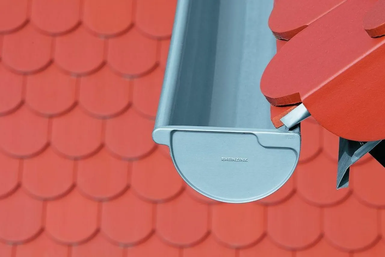 Fragment rynny tytan-cynk na tle czerwonego dachu.