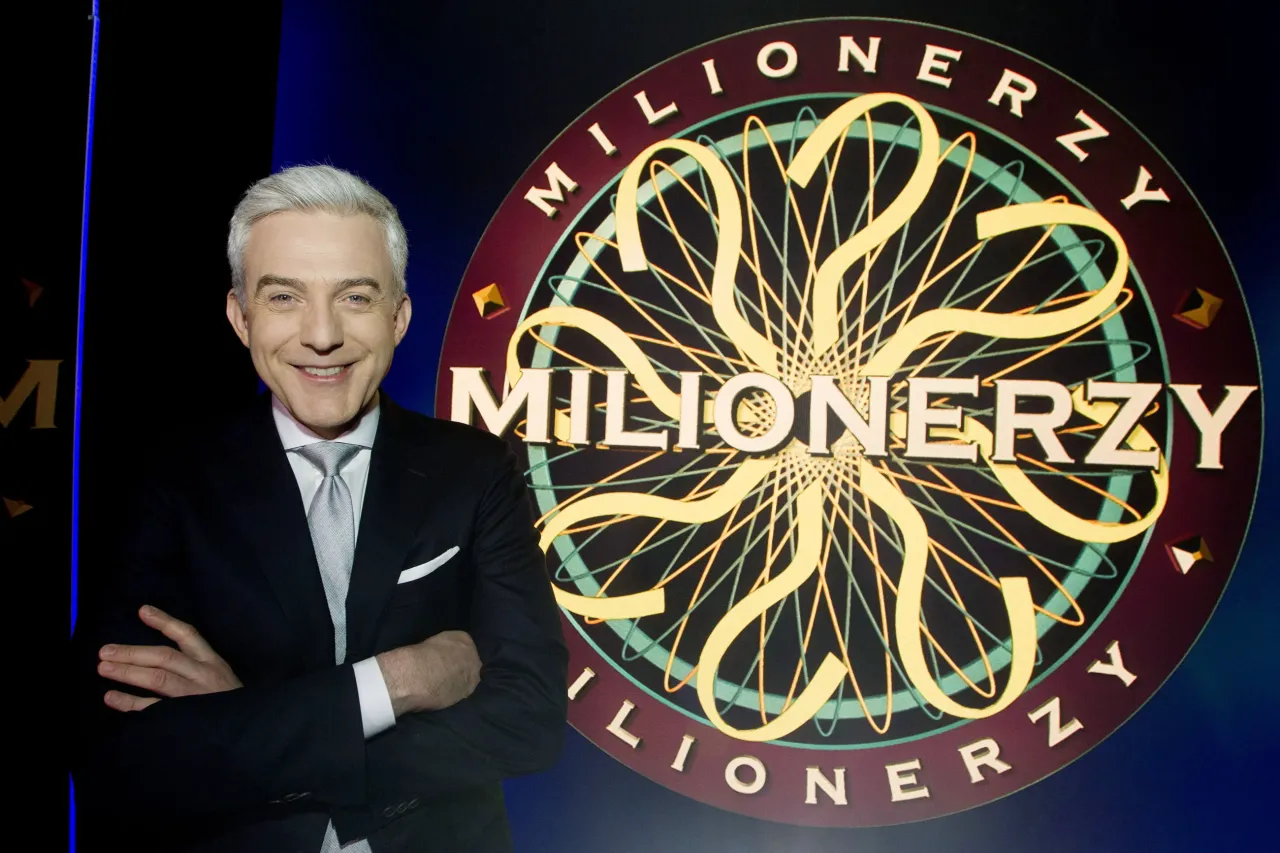 Uśmiechnięty Hubert Urbański stoi obok koła z pytajnikami z programu 