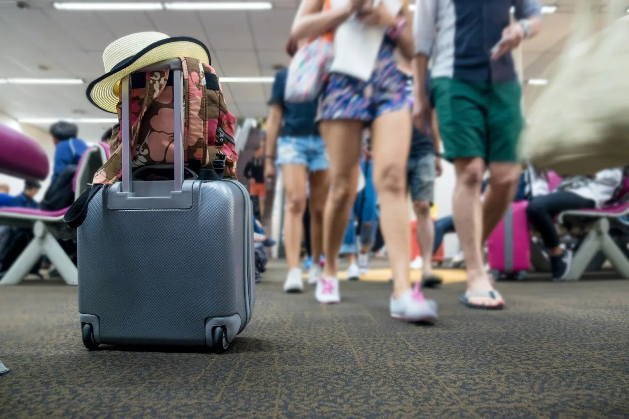 Walizka z plecakiem i kapeluszem na lotnisku. Ludzie w tle spieszą się na samolot, a Ty zastanawiasz się, co to turystyczny fundusz gwarancyjny.