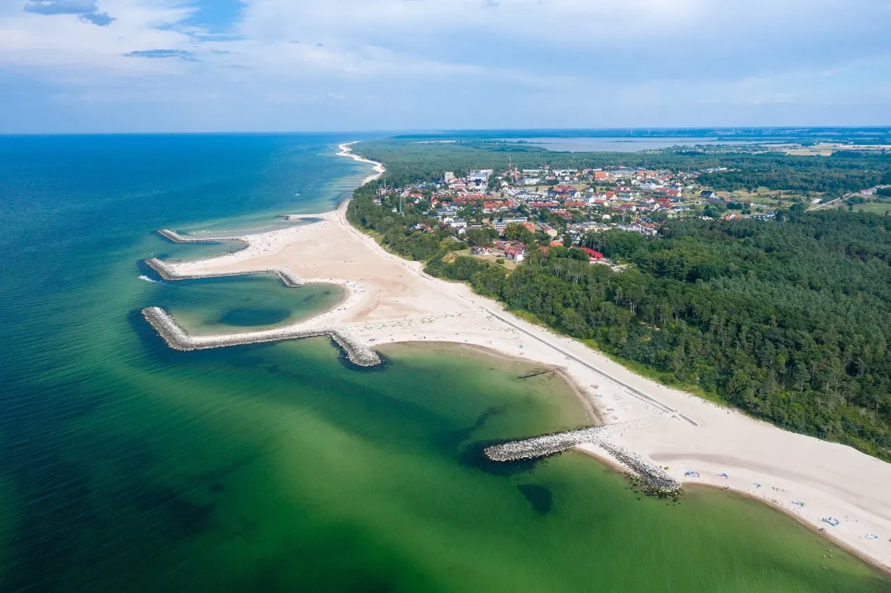 Widok z lotu ptaka na plażę i miasteczko. Widać falochrony, turkusową wodę i zabudowania. Tak wygląda Jarosławiec.