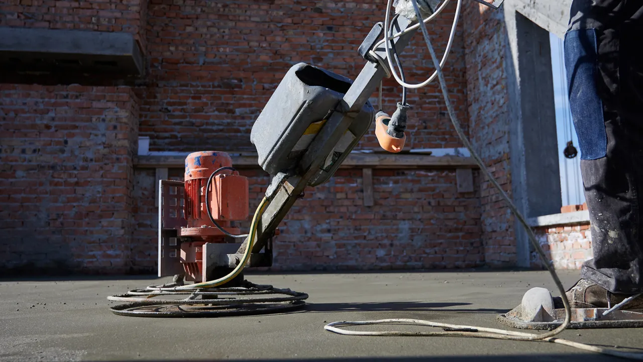 Tarka do betonu wygładza świeżą posadzkę. Maszyna z pomarańczowym silnikiem pracuje na budowie.