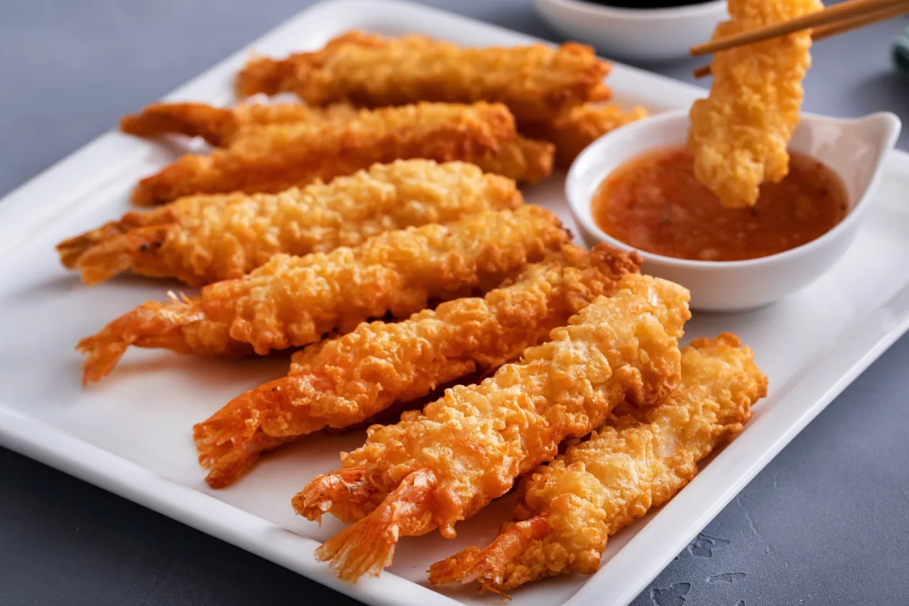 Chrupiące krewetki w cieście tempura, zanurzane w pysznym sosie. Idealne jako przekąska lub dodatek do dania.