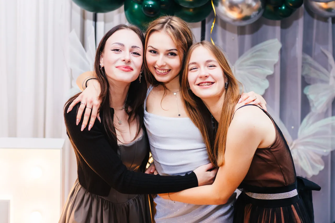 Trzy uśmiechnięte dziewczyny przytulają się na imprezie. Zastanawiasz się, ile kosztuje fotograf na 18?