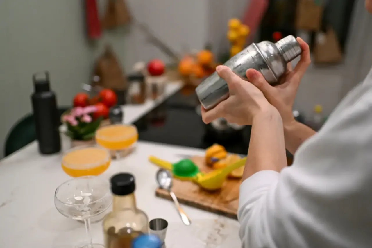 Ręce mieszają składniki w metalowym shakerze do drinków, przygotowując orzeźwiający koktajl.