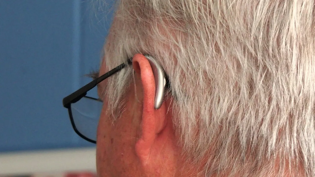 Pokazano, jak założyć aparat słuchowy. Urządzenie dyskretnie umieszczone za uchem, obok okular&oacute;w.