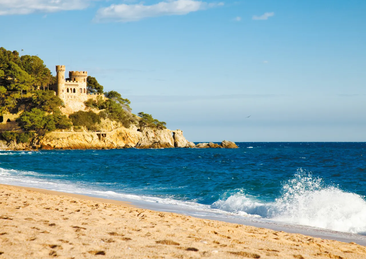 Zamek na klifie nad turkusowym morzem, piaszczysta plaża i fale. Takie widoki można zobaczyć w Hiszpanii.