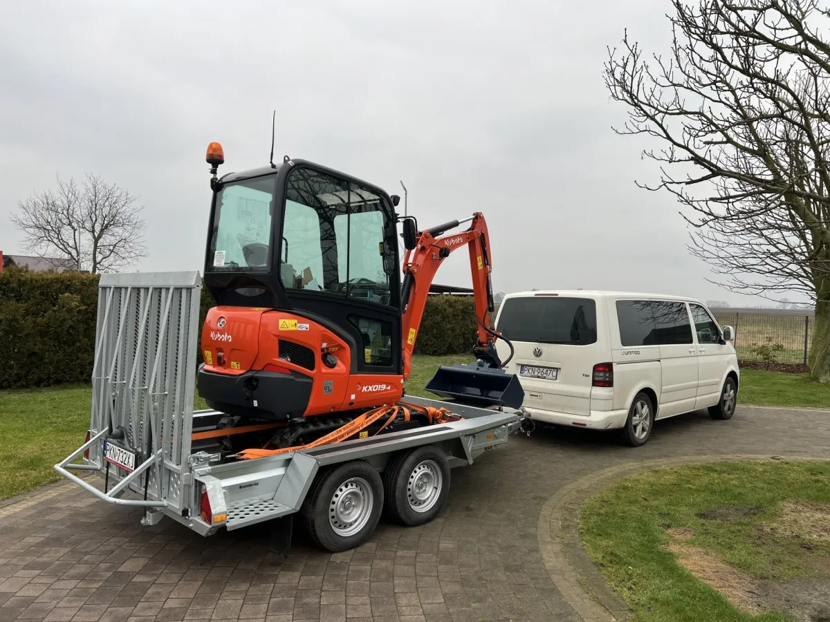Pomarańczowa mini koparka Kubota na przyczepie, gotowa do transportu. Zastanawiasz się, ile kosztuje mini koparka?