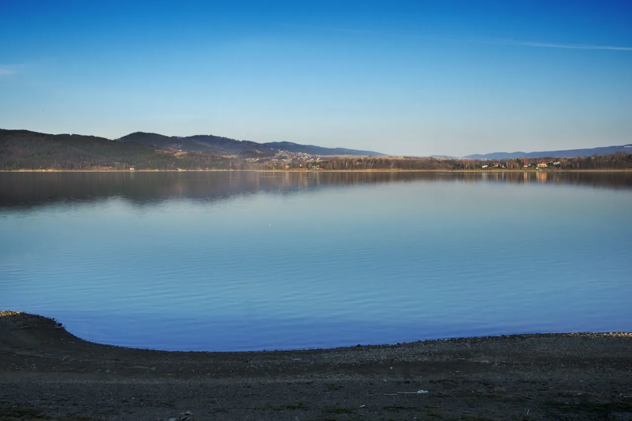 Spokojne jezioro z odbijającymi się w nim wzg&oacute;rzami i zabudowaniami. Idealne miejsce, by zastanowić się, co zwiedzić w Żywcu.