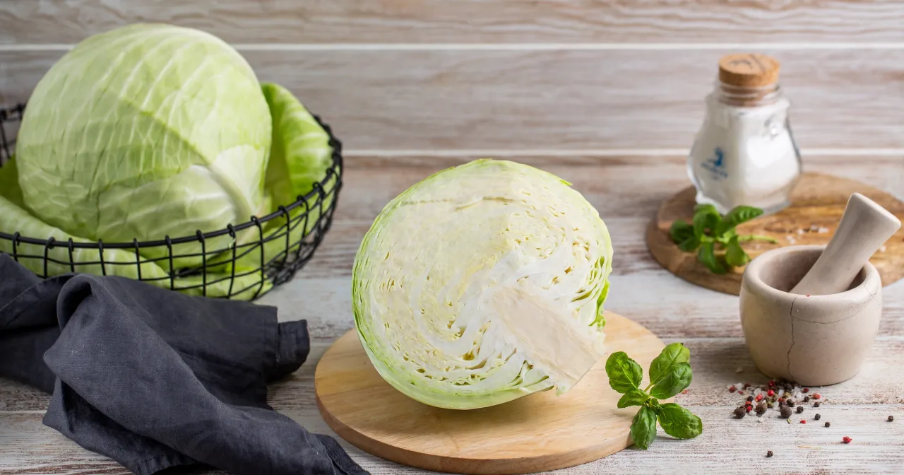 Świeża kapusta, czy surowa kapusta jest zdrowa? Na stole cała i przekrojona główka, koszyk z kapustą, moździerz i sól.