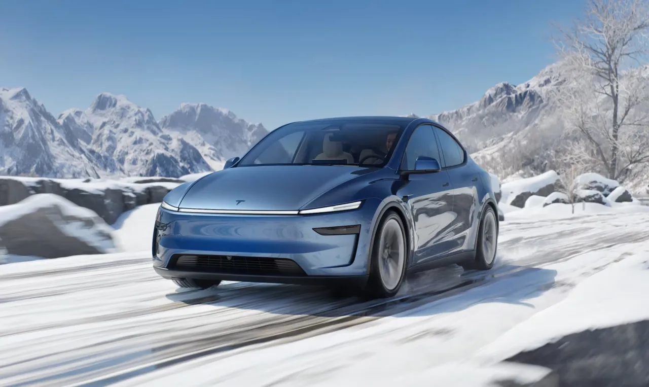 Niebieska Tesla jedzie po zaśnieżonej drodze w górach. Zastanawiasz się, ile Tesla ma zasięgu w takich warunkach?