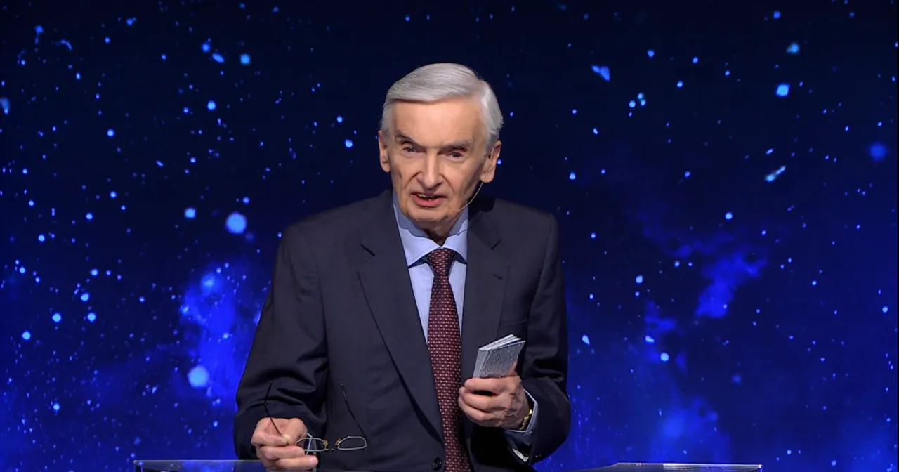 Stars twinkle behind a man in a suit, holding glasses and a small book. Jeden z dziesięciu od kiedy?