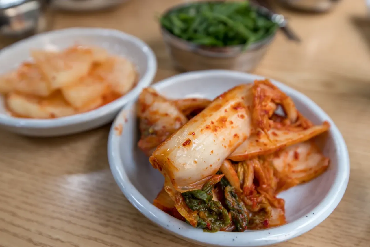 Kapusta kimchi co to jest? Pikantna, fermentowana kapusta pekińska w miseczce, obok innych koreańskich przystawek.