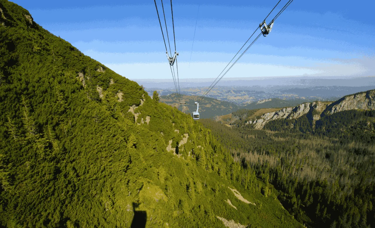 Kasprowy Wierch kolej wjeżdża na zielone zbocze Tatr. W oddali widać dolinę i pasmo górskie.