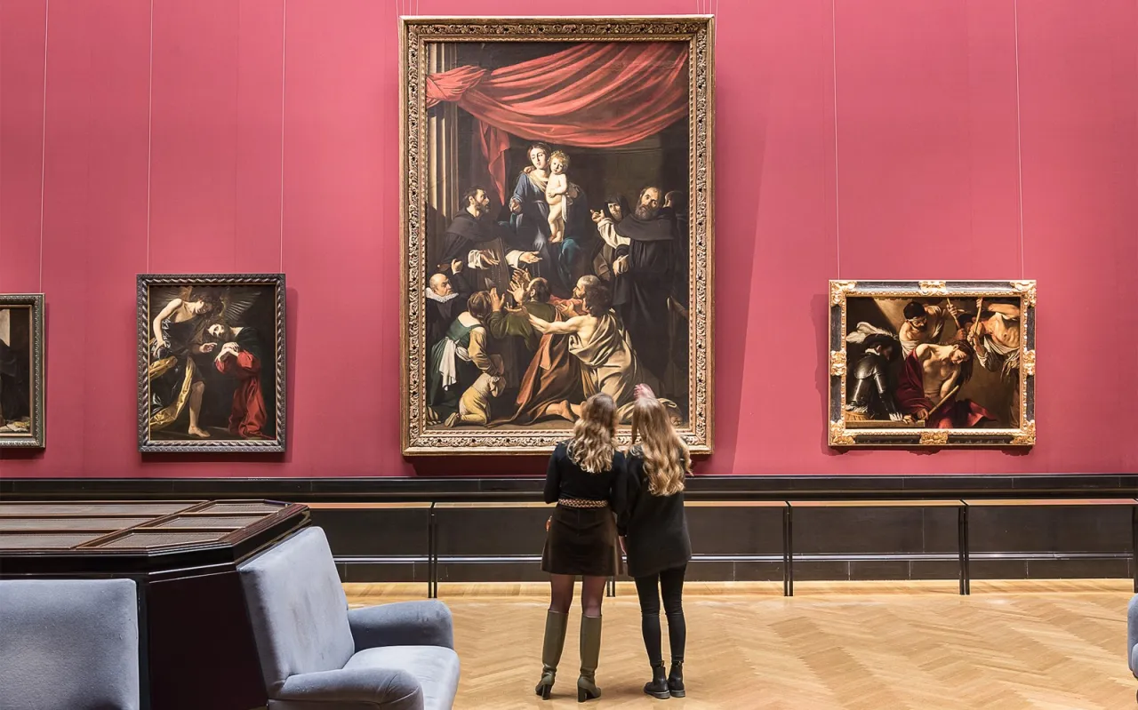 Dwie kobiety podziwiają obrazy w muzeum historii sztuki w Wiedniu. W centrum wisi wielkie płótno z Matką Boską i Dzieciątkiem, po bokach mniejsze dzieła.