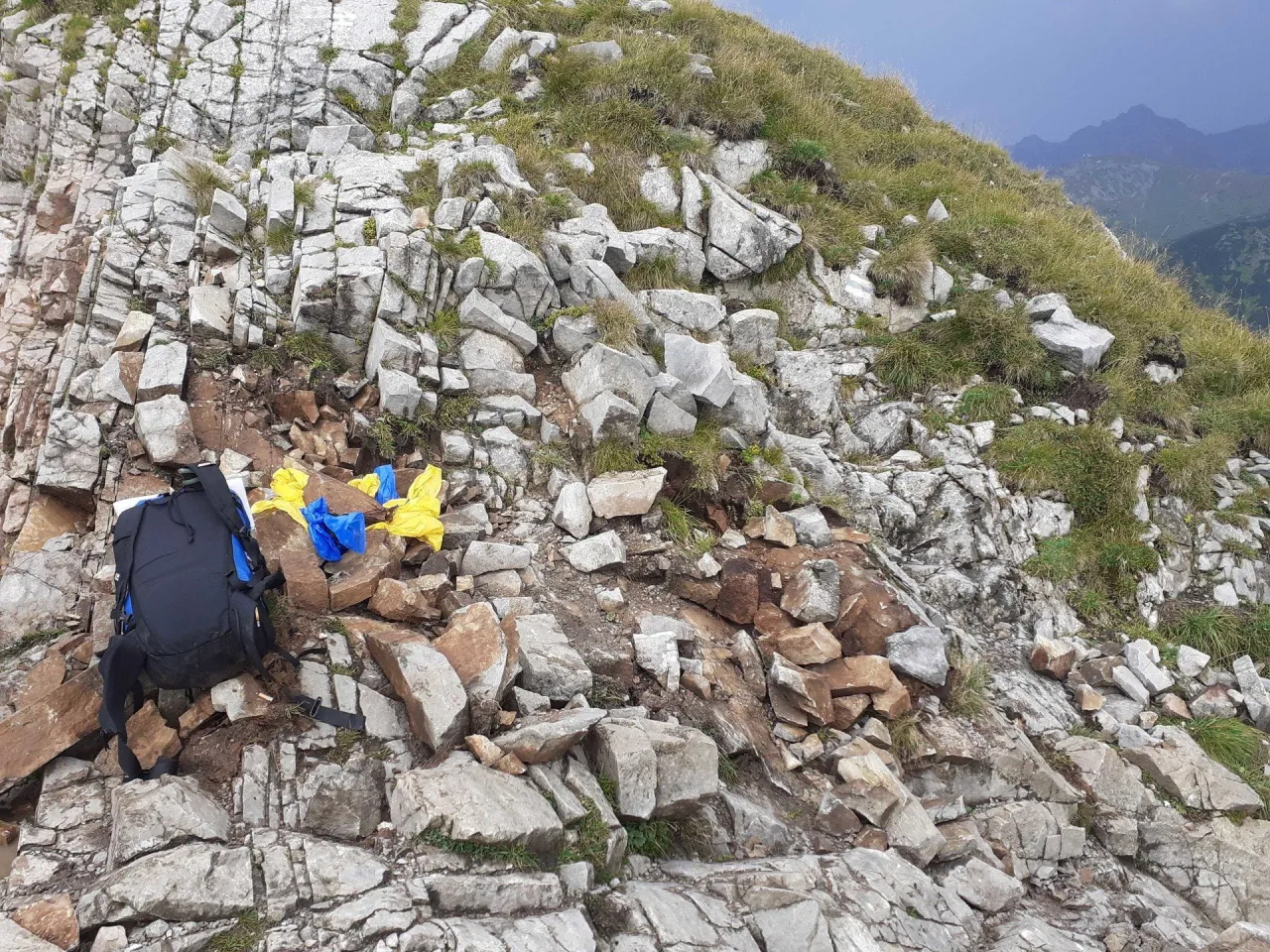 Plecak i kolorowe folie leżą na kamienistym zboczu Tatr. Wygląda jakby śpiący rycerz tatry odpoczywał po trudach wędrówki.