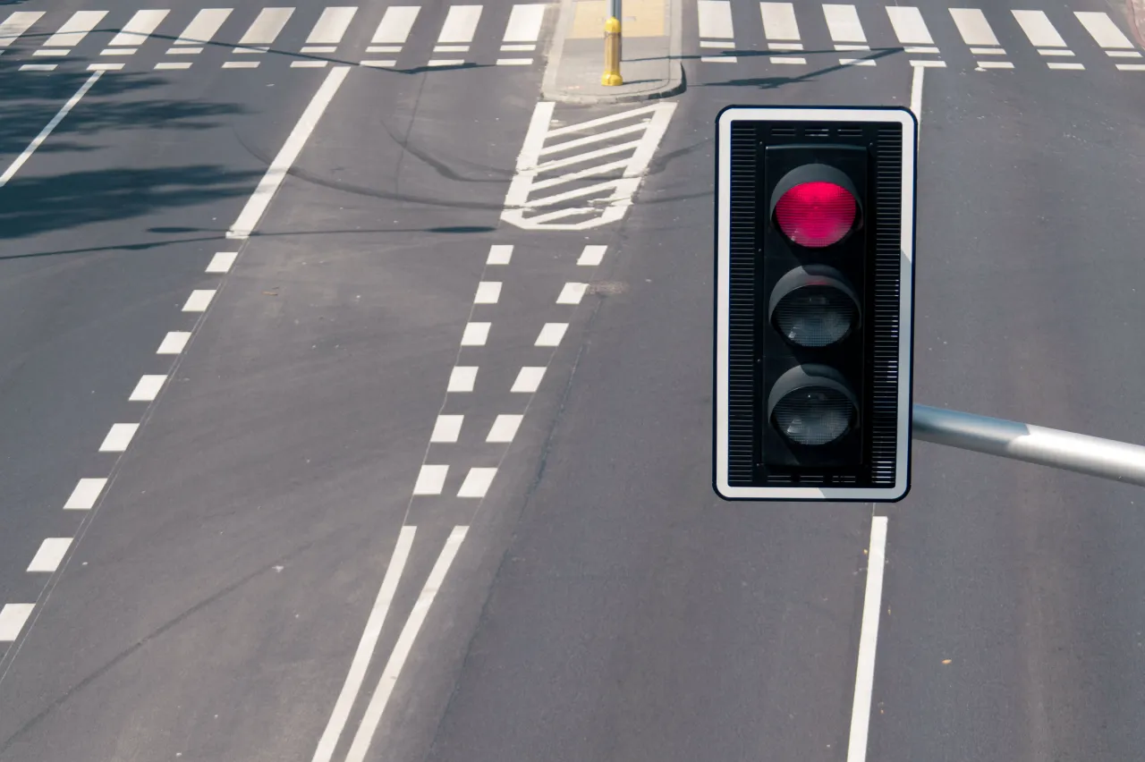 Czerwone światło sygnalizatora na skrzyżowaniu. Widoczne pasy dla pieszych i jezdnia. R&oacute;żne rodzaje kamer na skrzyżowaniach mogą monitorować ruch.
